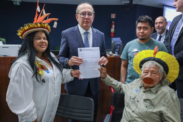 Fotografia colorida, na posição horizontal, do ministro Gilmar Mendes, da ministra Sonia Guajajara e do Cacique Raoni Matuktire. Os seguram juntos um documento.