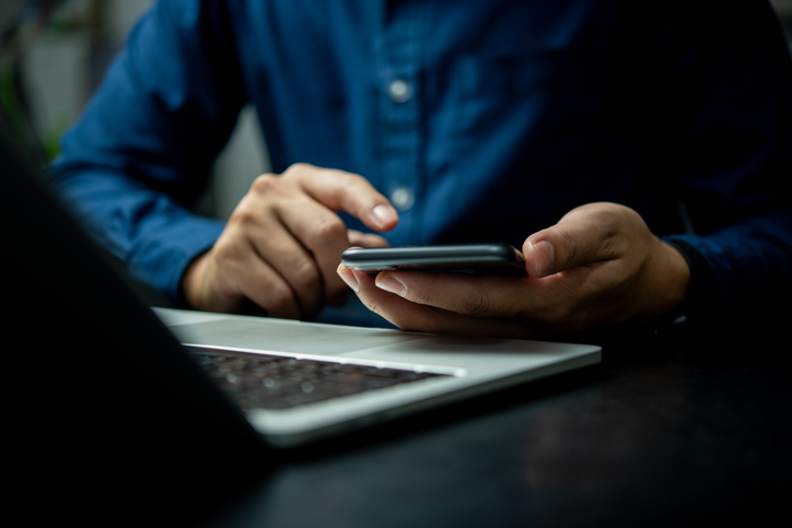A man is using a cell phone while sitting at a desk